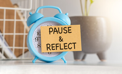 Written pause reflect with paper on alarm clock. Pause and reflect word with time concept.