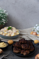 angerichteter Kartoffelsalat mit Frikadellen auf Tisch aus Holz mit Tuch und Blumen