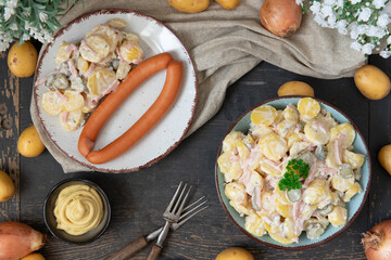 angerichteter Kartoffelsalat mit Wiener Würstchen auf Tisch aus Holz mit Tuch und Blumen