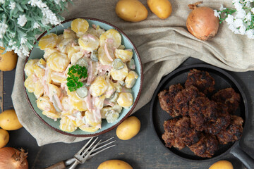 angerichteter Kartoffelsalat mit Frikadellen auf Tisch aus Holz mit Tuch und Blumen