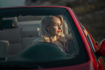 Gorgeous blonde in Hollywood style in an evening dress in a red convertible against the backdrop of...