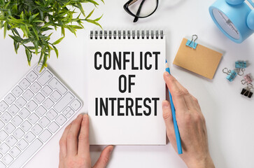 Conflict of interest text on blank business card being held by a woman's hand with blurred...