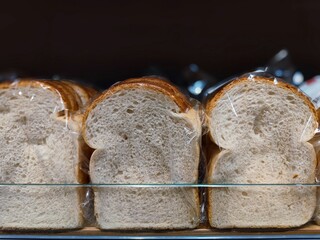 Unbranded slices of white bread wrapped in plastic are on a supermarket shelf ready to be sold in the shop at the bakery section