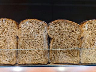 Unbranded slices of brown bread wrapped in plastic are on a supermarket shelf ready to be sold in the shop at the bakery section
