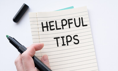 Obraz premium The words HELPFUL TIPS written on the notebook. Notebook in hand on a blue background.