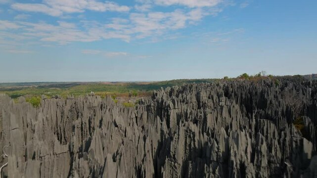 Camera gliding over the jagged peaks of Tsingy de Bemaraha National Park, a UNESCO World Heritage Site in Madagascar. The terrain features arid rocks and sparse vegetation