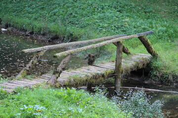 Rustic vintage dilapidated old narrow wooden bridge made of moss covered wooden logs and cracked...