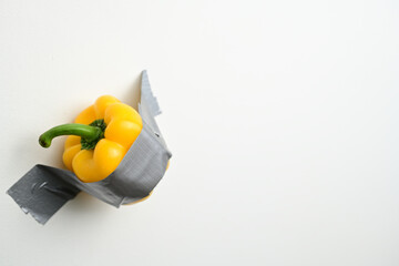 Yellow Bell Pepper Taped to Wall. A vibrant yellow bell pepper secured to a white wall with duct...