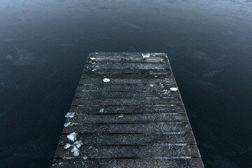 A frosty wooden pier leading to an icy lake under an overcast winter sky.