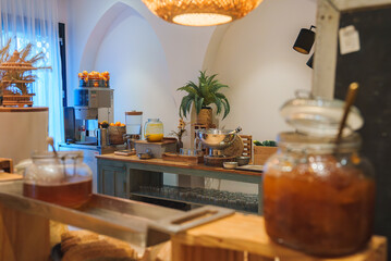 A wooden counter with glass jars, a juice dispenser, and fresh fruits in a Marrakech style hotel. Warm lighting and Moroccan decor enhance the ambiance.