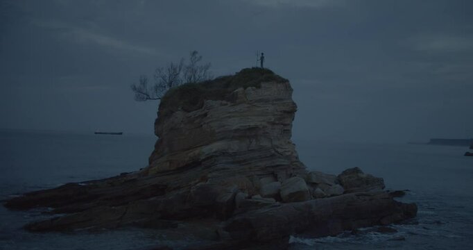 roca en medio del mar con una estatua de Poseid&oacute;n y de fondo un barco a un lado y del otro un acantilado