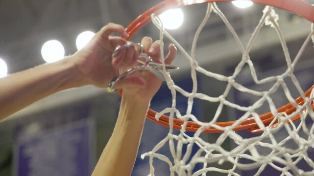 a closeup of a person's hand is seen cutting down a piece of the basketball net after winning a championship game