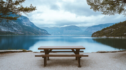Tranquil lakeside scene with a wooden picnic table surrounded by blue water, green mountains, and open sky, ideal for outdoor relaxation.