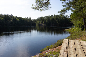Obraz premium calm lake in Muskoka Ontario Canada on bright day, water surrounded by trees with wooden dock in corner
