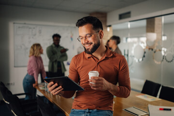 Smiling businessman using digital tablet and drinking coffee during a meeting in the office