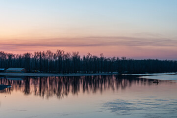 Obraz premium A tranquil winter view of the Dnipro River, showcasing its vast expanse under a serene sky, with faint silhouettes of Kyiv’s skyline and bridges in the distance.