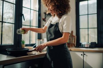 Woman chef pouring olive oil into frying pan in kitchen
