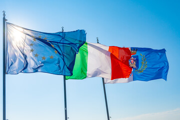 Three large waving flags of ITALY and EUROPEAN UNION and city of Terracina