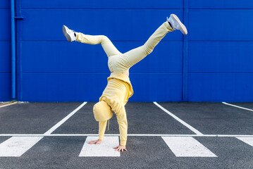 Yellow-dressed person in dynamic handstand near blue wall
