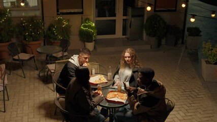 Group of friends enjoying pizza and drinks at outdoor table in cozy cafe during evening gathering