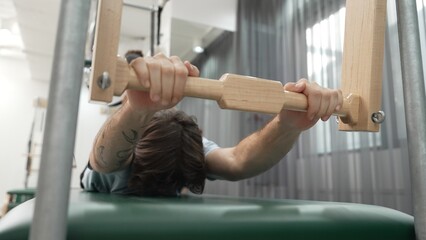 Man gripping pilates bar on reformer for upper body strength and control training during a workout...