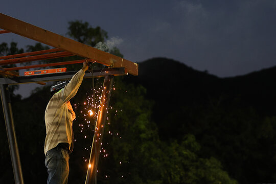 blacksmith welding metal structure at construction site at sunset