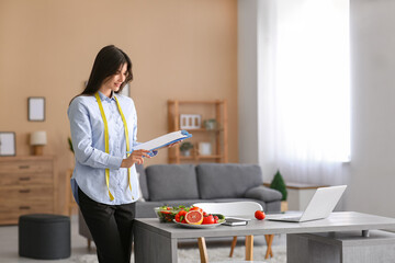 Beautiful nutritionist with clipboard in office