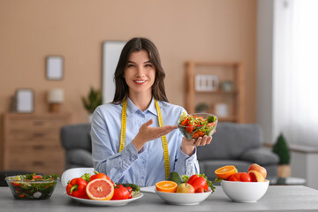 Beautiful nutritionist with vegetable salad at table in office
