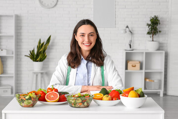 Young female nutritionist with healthy food on table in office