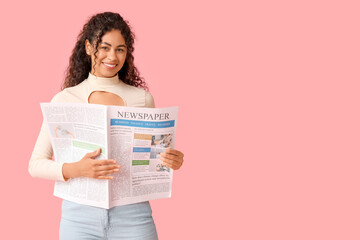 Happy young African-American woman with newspaper on pink background