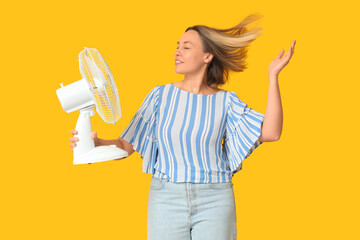 Beautiful mature happy woman with electric fan on yellow background