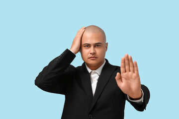 Bald businessman showing STOP gesture on blue background