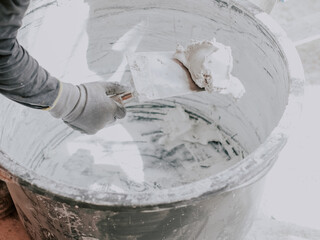 A young plasterer scoops up putty from a basin with a spatula.