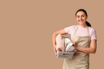 Beautiful young happy woman with basket of clean towels on beige background