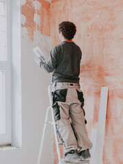A young caucasian guy applies fresh putty with a small spatula on the wall near the window