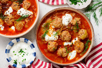 Romanian Cabbage Soup with Meatballs, Tomatoes and Sour Cream in a ceramic bowl on a table.  .style hugge