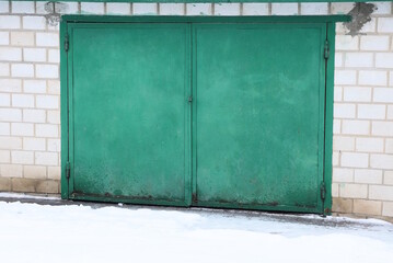 one big closed green metal gate on a brick wall of a garage in the street in white snow