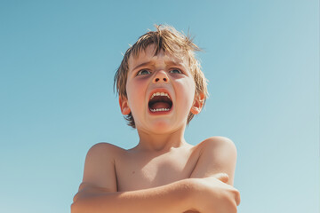Angry shirtless boy with arms crossed, shouting dramatically against a bright blue sky. Expressive child shows strong emotions and defiant personality on a sunny summer day