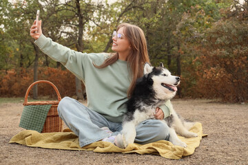 Beautiful young woman with cute Husky dog taking selfie on picnic in park