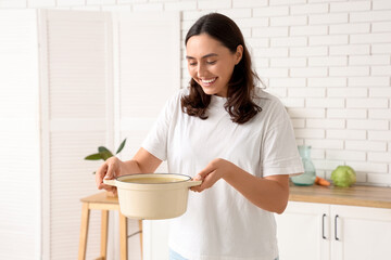 Young woman holding cooking pot with tasty soup in kitchen