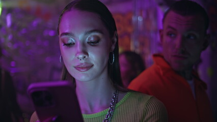 Smiling clubber looking cellphone in neon light nightclub closeup. Woman texting