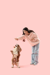 Obraz premium Beautiful young woman playing with cute cavalier King Charles spaniel on pink background