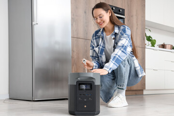 Young woman connecting fridge to portable power station in kitchen