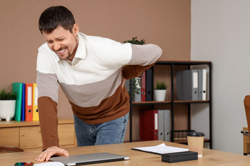 Young man suffering from back pain in office