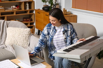 Beautiful young happy female composer with laptop playing synthesizer at home