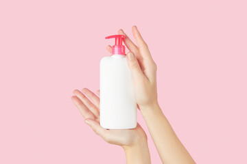Womans hands holding white bottle on pastel pink background