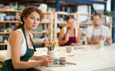 Woman learns to make designs on clay plate using brush and paint in a pottery workshop