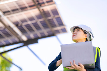 Engineer in safety vest and helmet pointing towards a solar powered carport, illustrating...