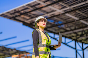 Fototapeta premium Engineer in safety vest and helmet pointing towards a solar powered carport, illustrating eco-friendly innovation in parking infrastructure. Solar panels provide shade and sustainable energy.