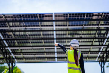 Engineer in safety vest and helmet pointing towards a solar powered carport, illustrating...